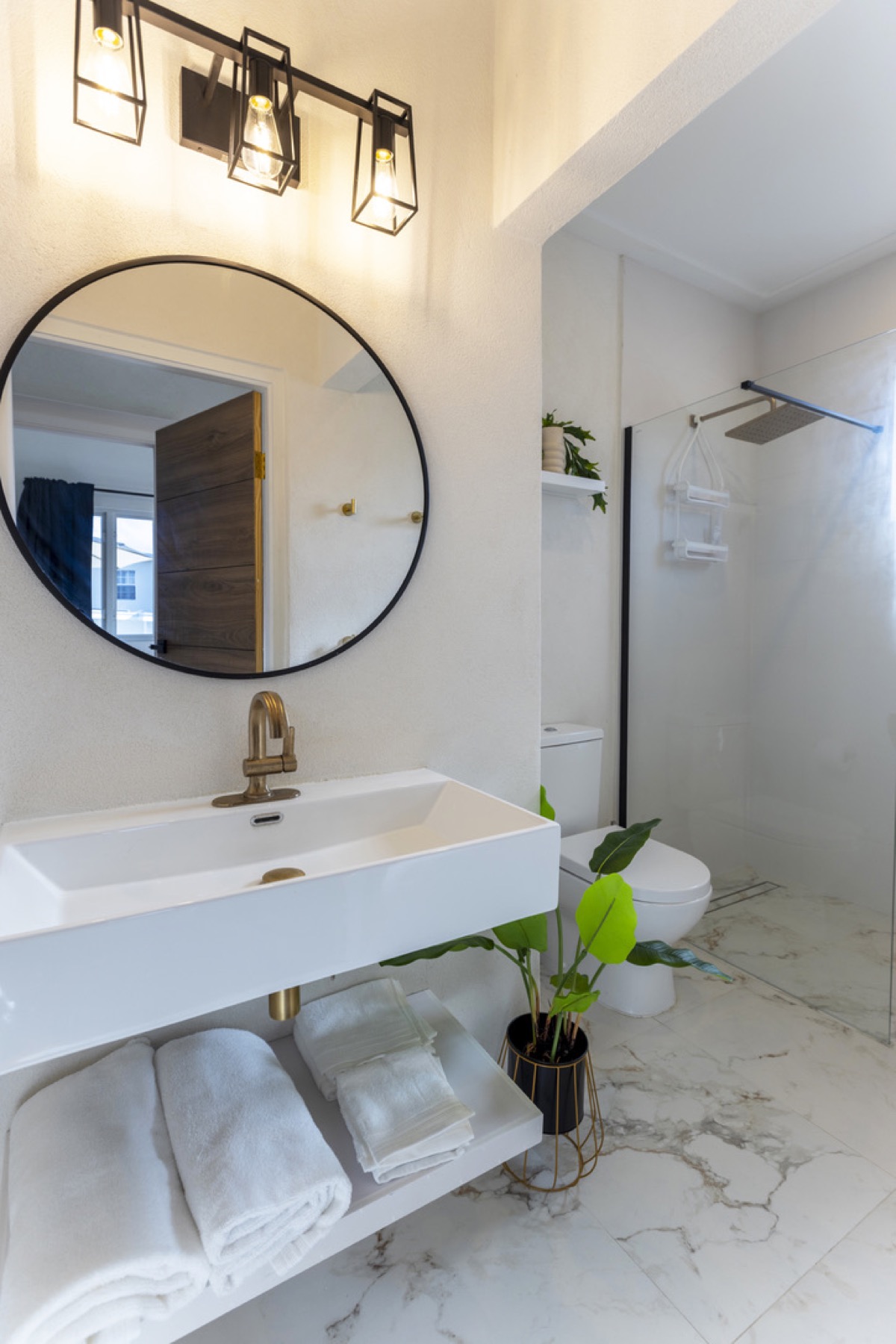 Shared bathroom — marble, brass tap, round mirror, cage vanity lights