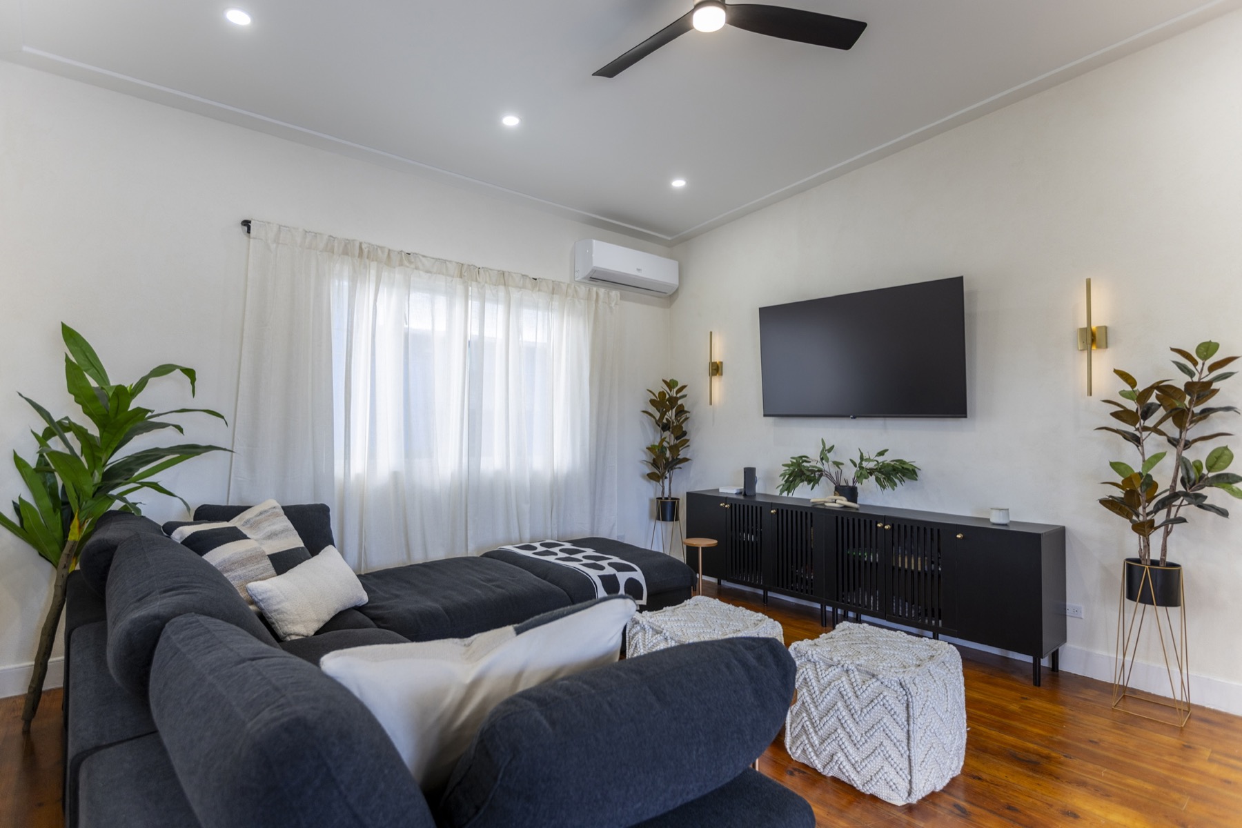 Lounge — charcoal sectional, brass sconces, sheer curtains, dark hardwood
